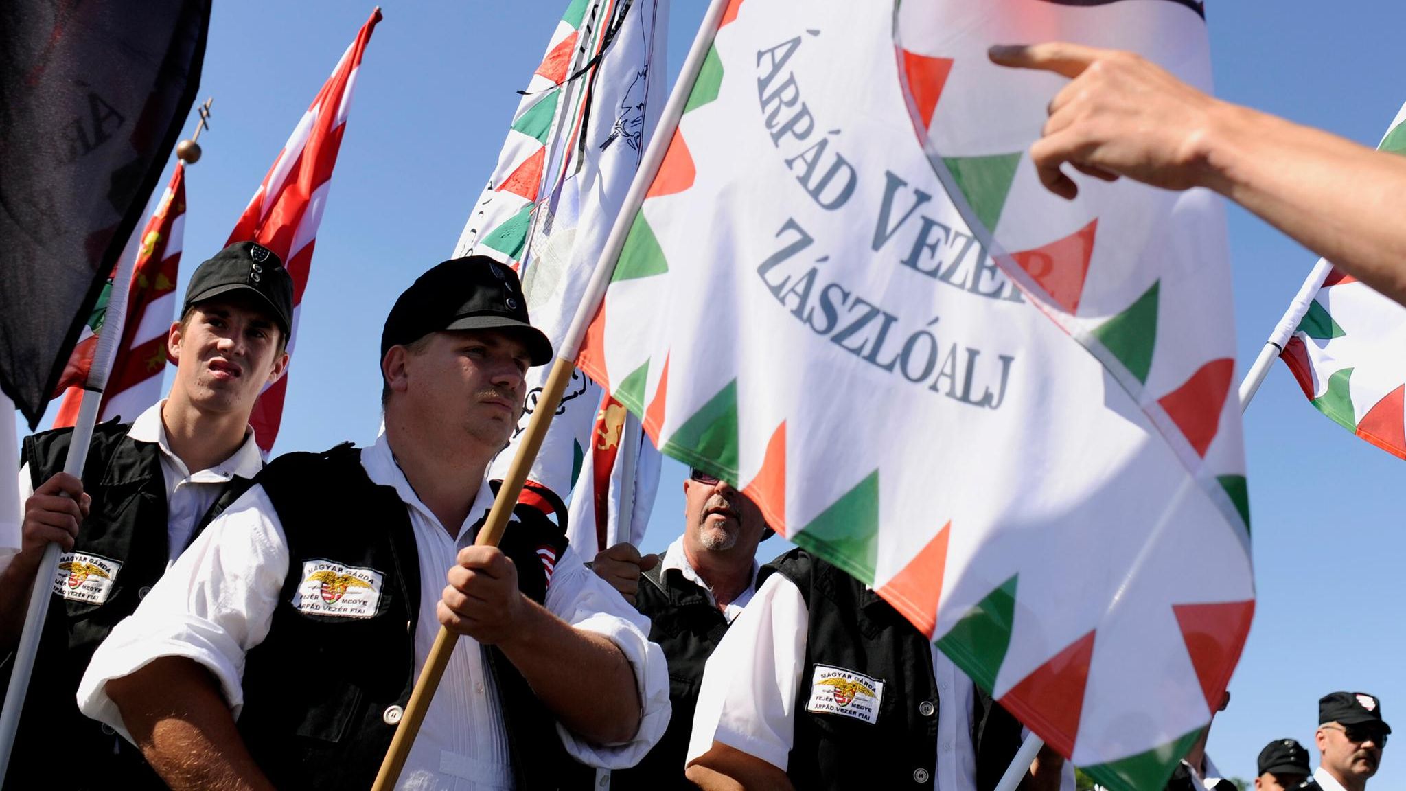 Eine Gruppe von Männern marschiert mit Fahnen im Sonnenlicht