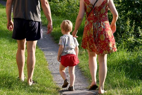 Kindergeld Symbolbild: Ein Kind geht einen Waldweg inmitten der Eltern entlang