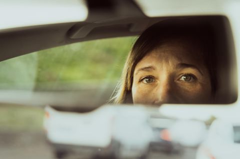 Frau guckt in den Rückspiegel ihres Autos mit Angst vor dem Autofahren