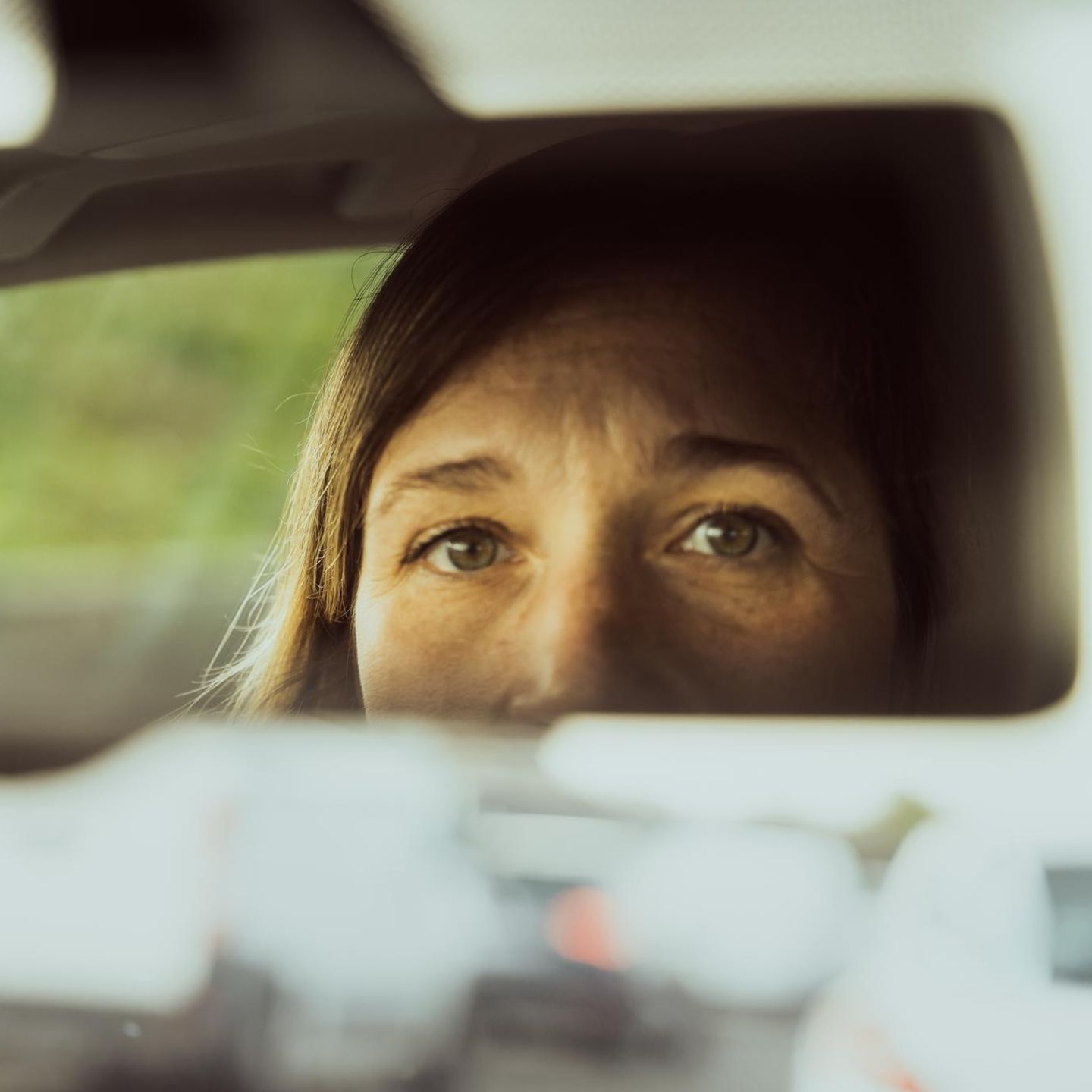 Frau guckt in den Rückspiegel ihres Autos mit Angst vor dem Autofahren