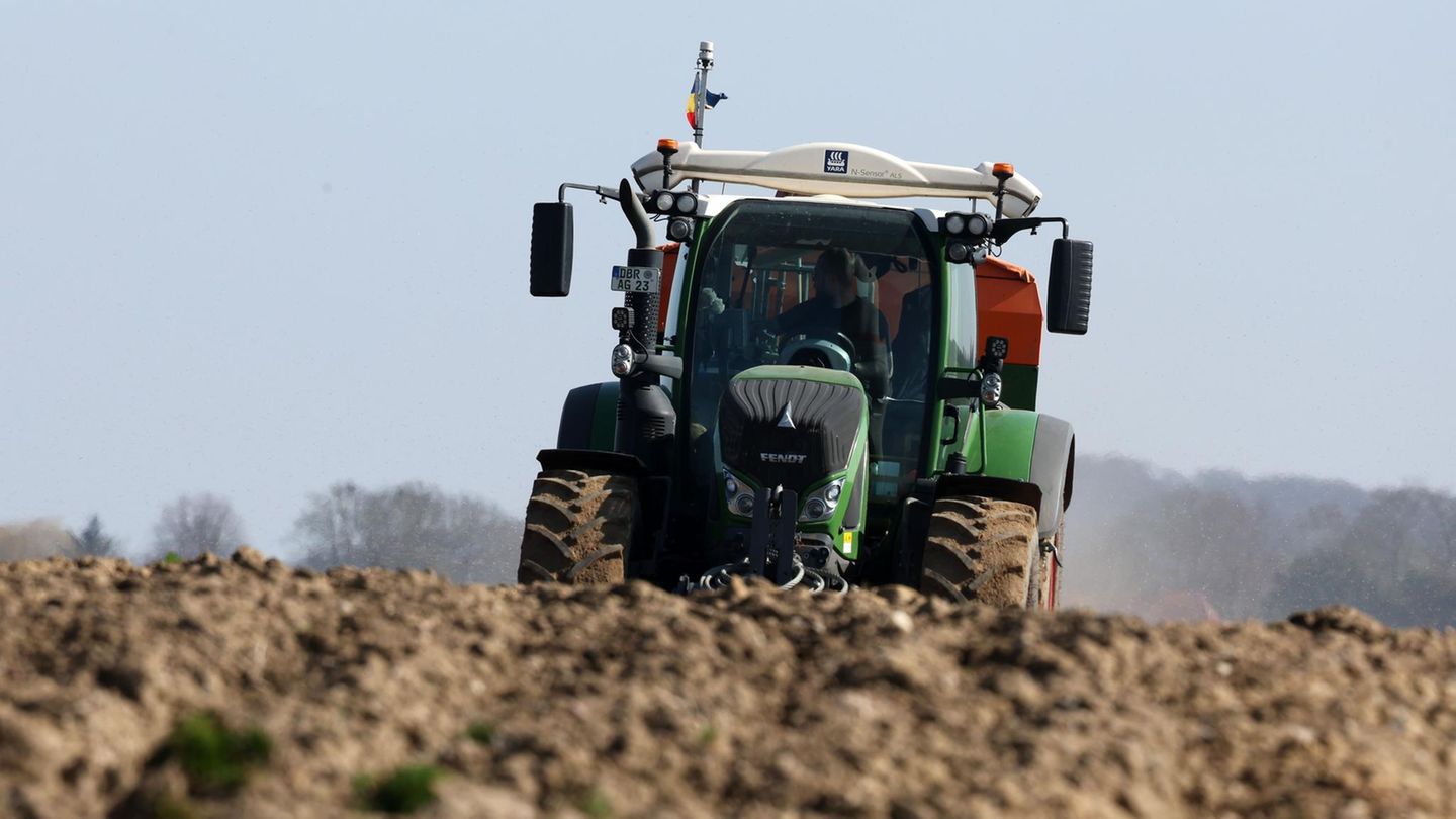 Ein Landwirt fährt in einem grünen Traktor über einen leeren Acker