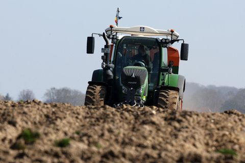 Ein Landwirt fährt in einem grünen Traktor über einen leeren Acker