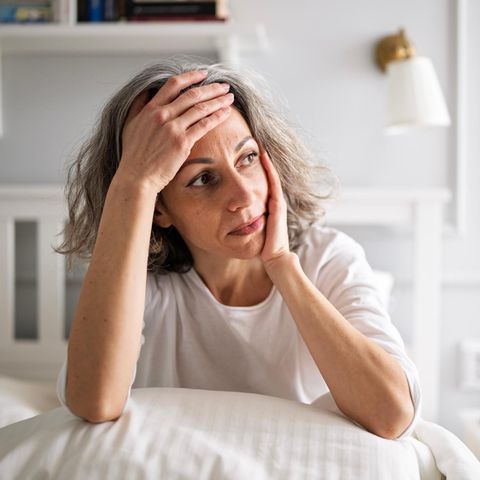 ADHS: Frau sitzt im Bett und grübelt mit Hand an der Stirn