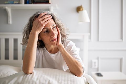 ADHS: Frau sitzt im Bett und grübelt mit Hand an der Stirn