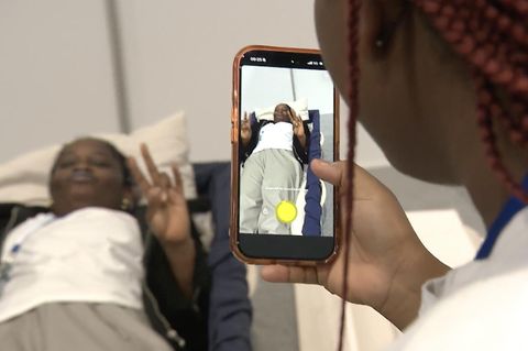 Ein Handy fotografiert eine Person im Sarg mit Peacezeichen