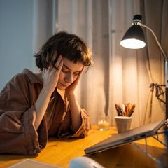 Lohnfortzahlungen im Krankheitsfall: Eine Frau reibt sich den Kopf und sitzt am Schreibtisch