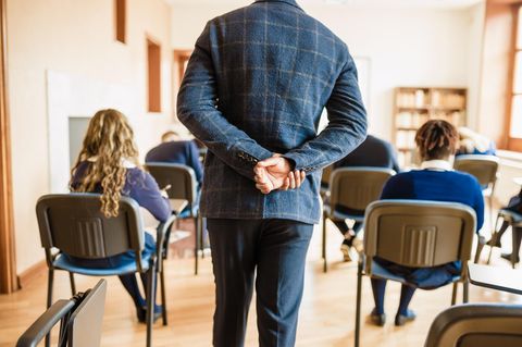 Lehrkraft von hinten. Er hat die Arme auf dem Rücken verschränkt. Narzissmus kommt auch bei Lehrkräften vor.