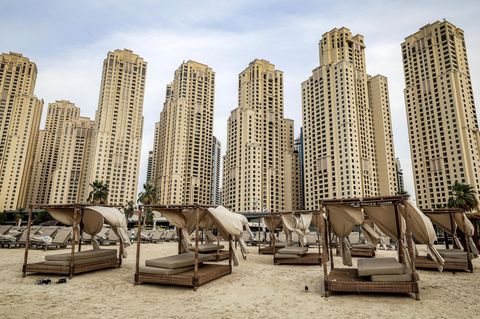 Leere Sonnenbetten an einem leeren Strand vor gelben Wolkenkratzern in Dubai