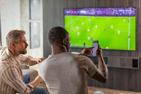 Zwei Männer schauen Fußball und wetten dabei auf dem Smartphone – mit ChatGPT?