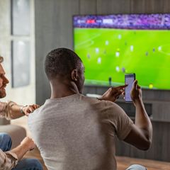 Zwei Männer schauen Fußball und wetten dabei auf dem Smartphone – mit ChatGPT?