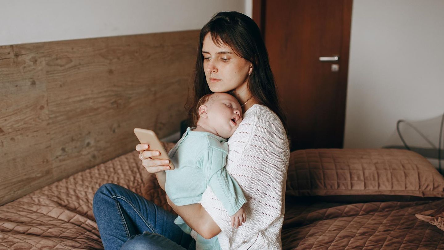 Stillen: Eine Mutter hält ihr Baby in den Armen und blickt dabei auf ihr Handy