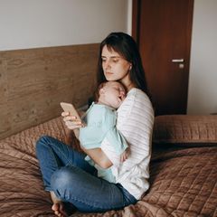 Stillen: Eine Mutter hält ihr Baby in den Armen und blickt dabei auf ihr Handy