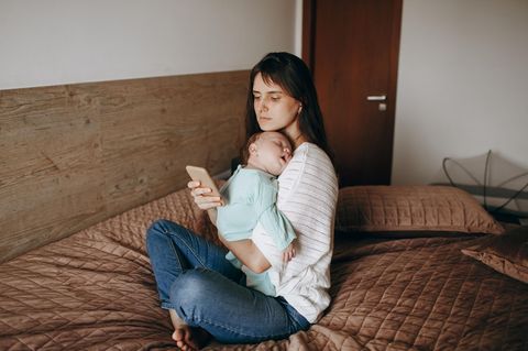 Stillen: Eine Mutter hält ihr Baby in den Armen und blickt dabei auf ihr Handy