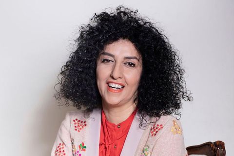 Narges Mohammadi sitzt lächelnd auf einem Stuhl vor einer weißen Wand