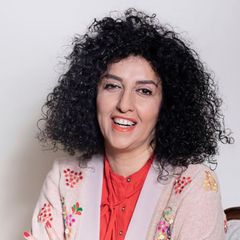 Narges Mohammadi sitzt lächelnd auf einem Stuhl vor einer weißen Wand