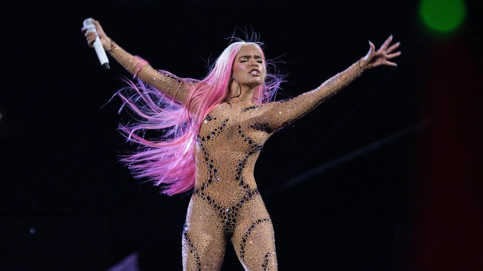 Karol G hat bei einer Performance auf der Bühne die Augen geschlossen und reckt die Arme in die Luft