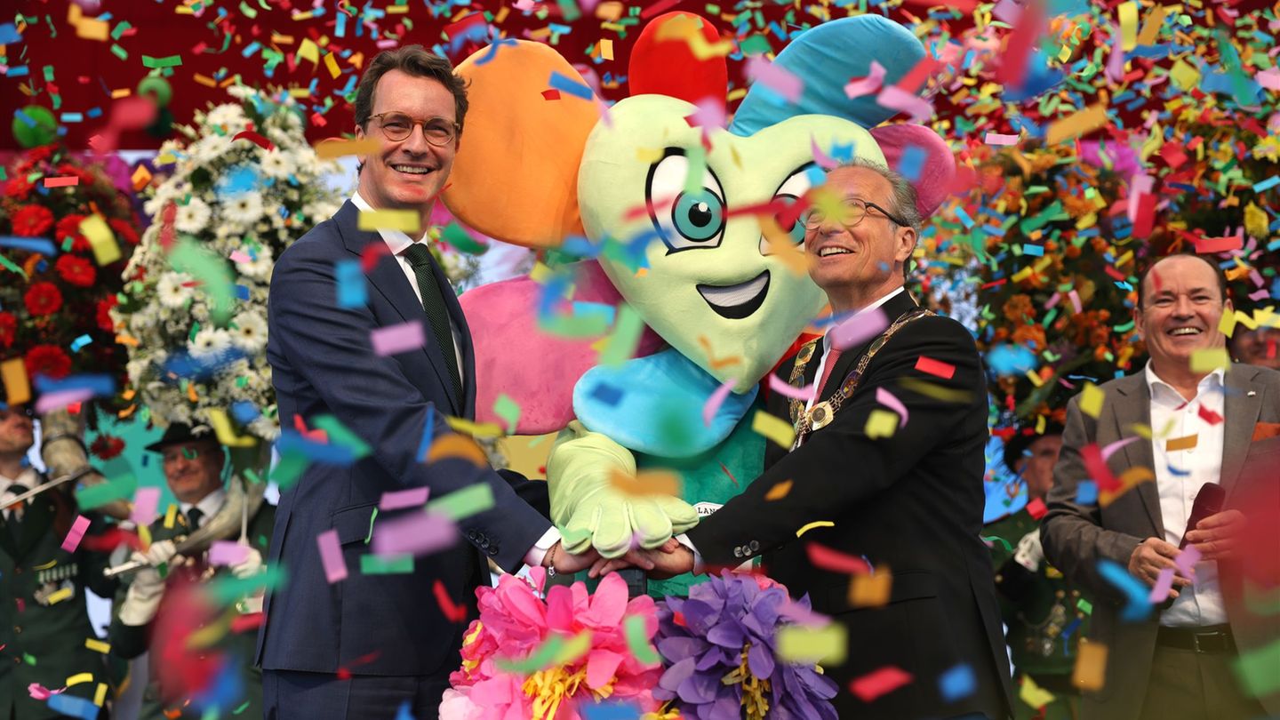 Moderator Wolfram Kons (r) steht neben Ministerpräsident Hendrik Wüst (l, CDU) und Bürgermeister Reiner Breuer (m, SPD) auf der