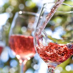 Weingläser, in die ein rötlicher Wein eingeschenkt wird, im Hintergrund Bäume leicht unscharf