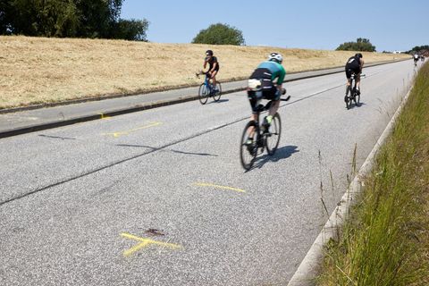Triathleten fahren auf dem Rad an der Unglücksstelle auf dem Gauerter Hauptdeich vorbei. Foto: Georg Wendt/dpa