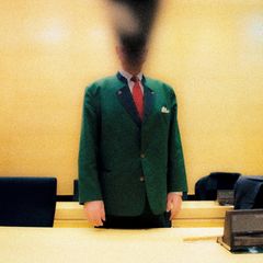 Der Angeklagte steht mit einem grünen Jacket vor Gericht. Sein Gesicht ist unkenntlich