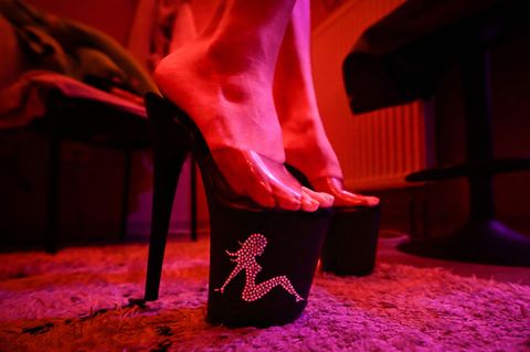 Die Füße einer Prostituierten in Plateau High Heels werden von rötlichem Licht beschienen, Symbolbild Skandal in Italien
