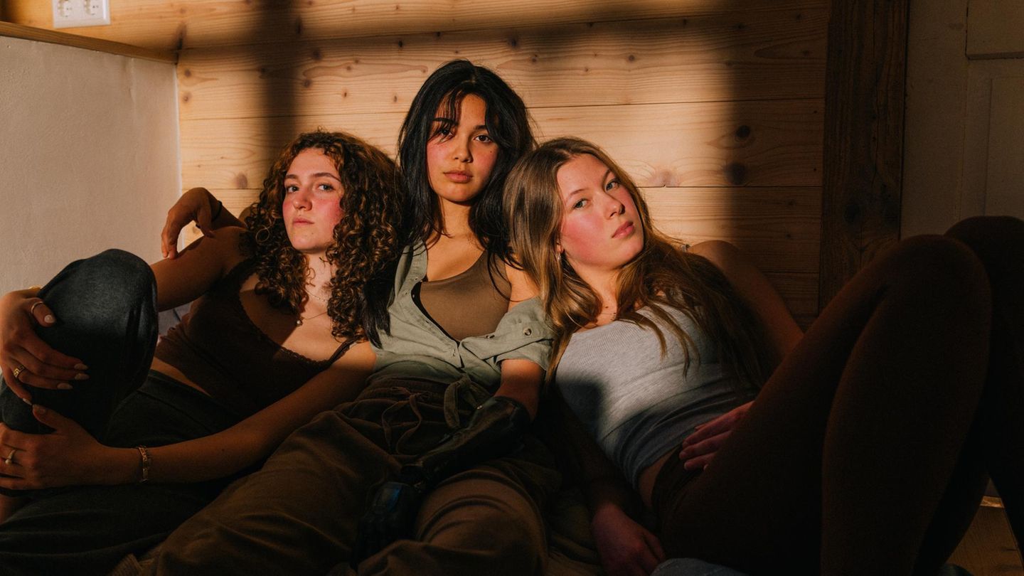 Drei junge Leute der Gen Z sitzen entspannt auf dem Boden und blicken in die Kamera