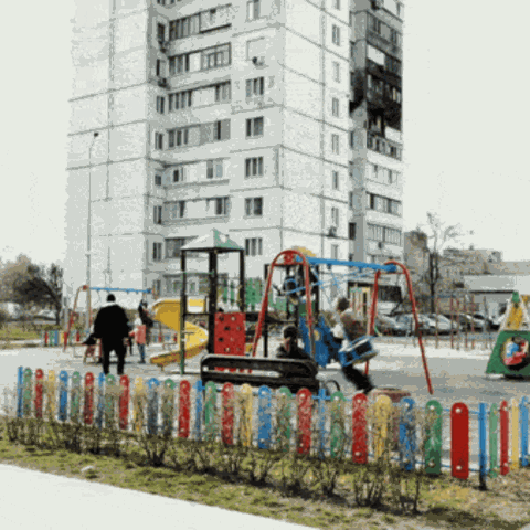 Kinder auf einem Spielplatz vor einem Hochhaus, in das eine Drohne eingeschlagen ist