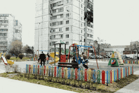 Kinder auf einem Spielplatz vor einem Hochhaus, in das eine Drohne eingeschlagen ist