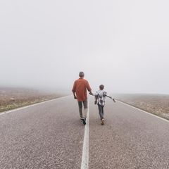 Symbolfoto Suizid: Vater und Sohn gehen auf einer Straße dem Horizont entgegen