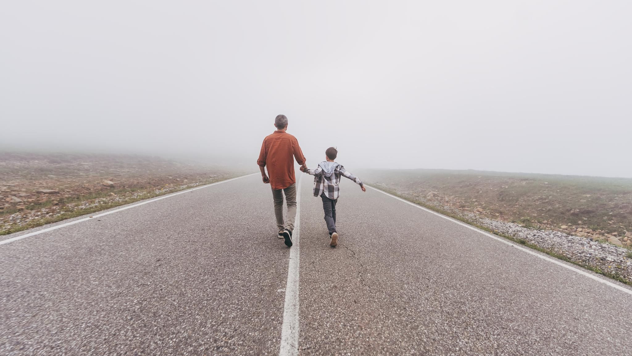Symbolfoto Suizid: Vater und Sohn gehen auf einer Straße dem Horizont entgegen
