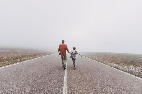 Symbolfoto Suizid: Vater und Sohn gehen auf einer Straße dem Horizont entgegen