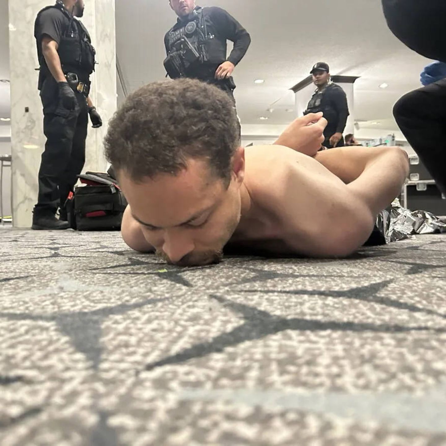 Ein Mann liegt mit nacktem Oberkörper und hinter dem Rücken gefesselten Händen auf dem Boden