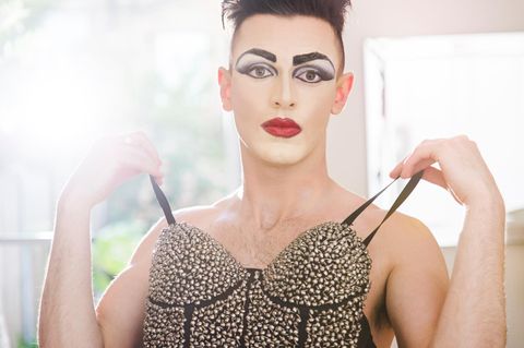 Fetisch Crossdressing: Ein geschminkter Mann hält eine Corsage vor seinen nackten Oberkörper
