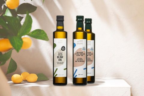 Drei Flaschen Olivenöl stehen auf einem Tisch vor einer beigefarbenen Wand