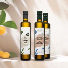 Drei Flaschen Olivenöl stehen auf einem Tisch vor einer beigefarbenen Wand