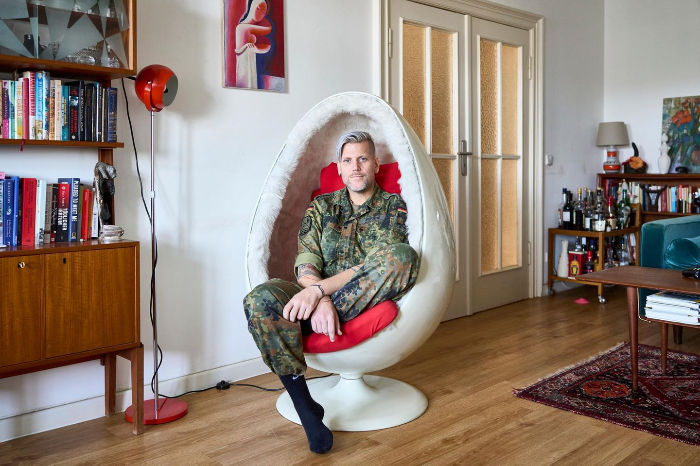 Ein Porträt von einer Transfrau in Bundeswehr Uniform, sitzt in einer Wohnung