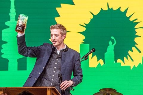 Dominik Krause hebt am Rednerpult eine Maß Bier.