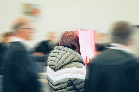 Die Angeklagte trägt eine grüne Jacke und hält sich einen roten Ordner vors Gesicht, sie ist von hinten fotogafiert.