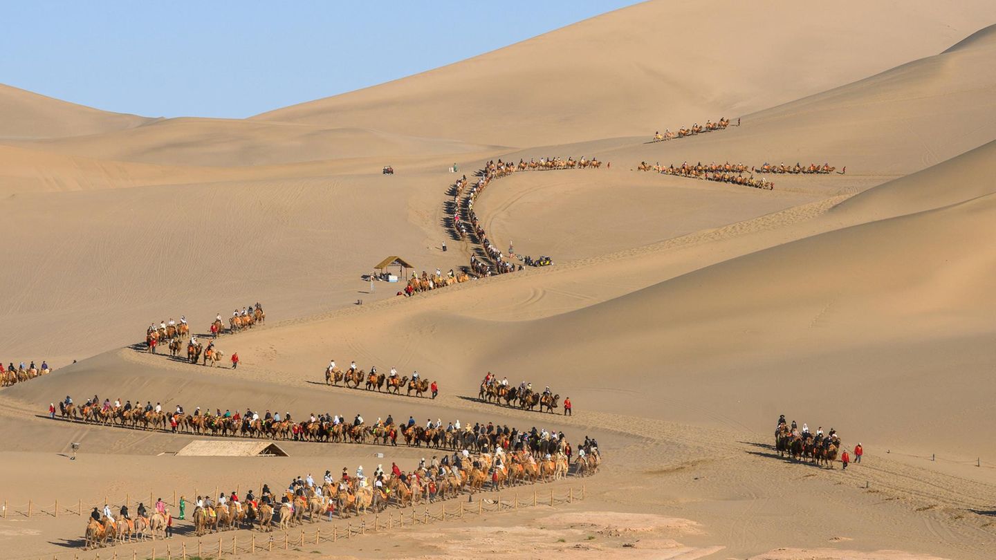 Dunhuang, China. Mit einer exklusiven Safari hat das nichts zu tun: Tausende Touristen reiten Kamelen zum Mingsha-Berg. Das erste Maiwochenende steht in China im Zeichen des Tags der Arbeit. In diesem Jahr nutzen viele das verlängerte Wochenende für einen Kurzurlaub oder Ausflüge.