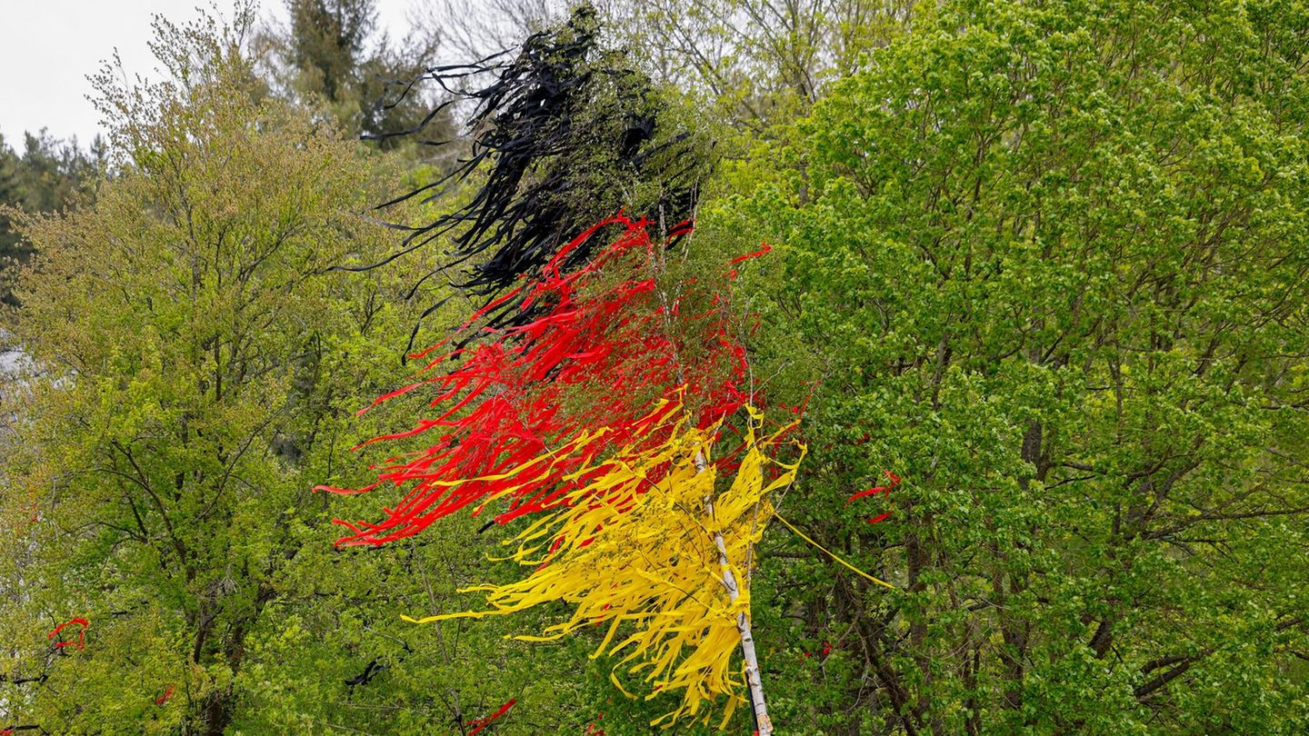 Schleiden, Deutschland. Ein Maibaum, geschmückt mit Bändern in den Farben Schwarz, Rot und Gold, steht auf einem Platz. 