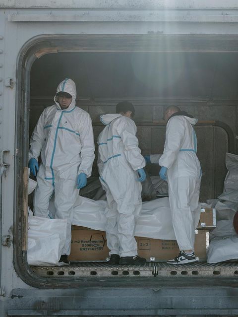 Forensiker in Schutzanzügen in Odessa, Ukraine, hinter ihnen Leichensäcke