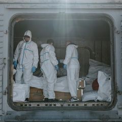 Forensiker in Schutzanzügen in Odessa, Ukraine, hinter ihnen Leichensäcke