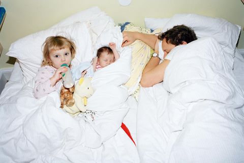 Ein erschöpfter Vater liegt mit seinen Kindern im Bett