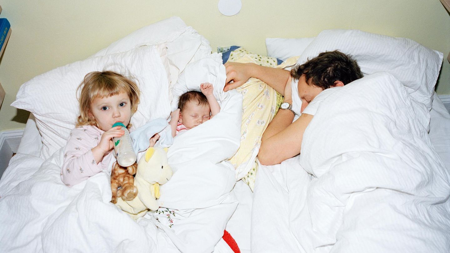 Ein erschöpfter Vater liegt mit seinen Kindern im Bett