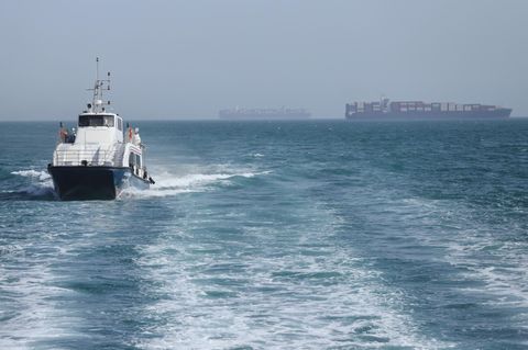 Ein iranisches Patrouillenboot fährt durch die Straße von Hormus, während Frachtschiffe vor Bandar Abbas vor Anker liegen