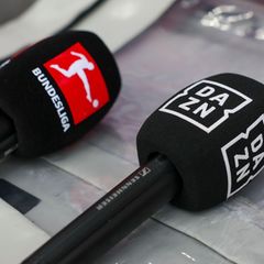 Mikrofone mit den Logos von Bundesliga und Dazn liegen auf einer Box