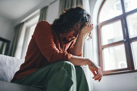Eine junge Frau sitzt überfordert auf dem Bett