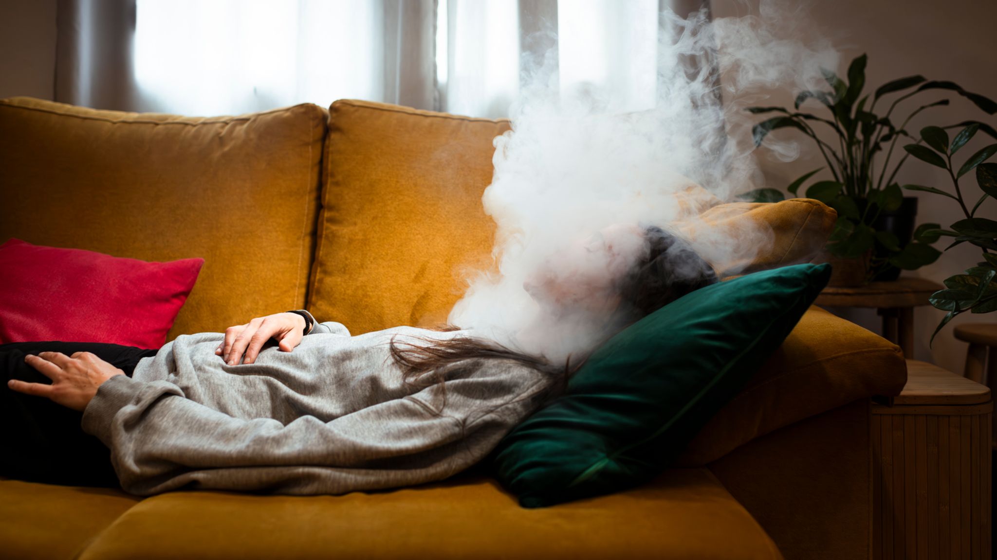 Nebel im Gehirn – Brainfog Symbolbild: Eine Person liegt auf einer gelben Couch, ihr Kopf ist von Nebel umhüllt