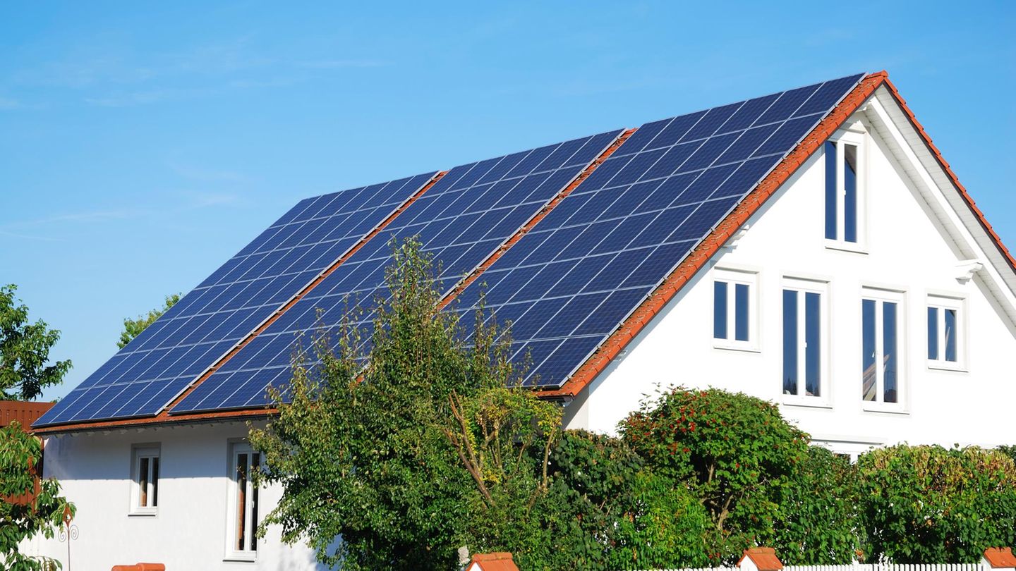 Solarmodule auf dem roten Dach eines weißen Einfamilienhauses, im Hintergrund blauer Himmel