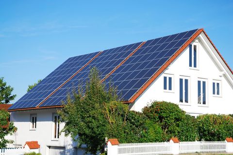 Solarmodule auf dem roten Dach eines weißen Einfamilienhauses, im Hintergrund blauer Himmel
